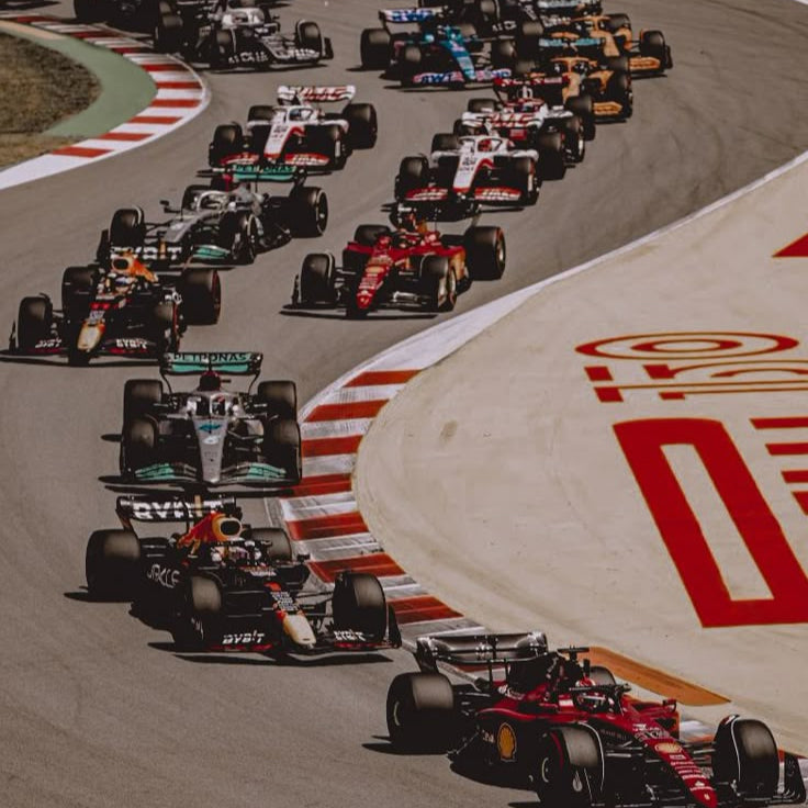 Formula 1 cars racing on a track with a prominent red and white logo on the side.
