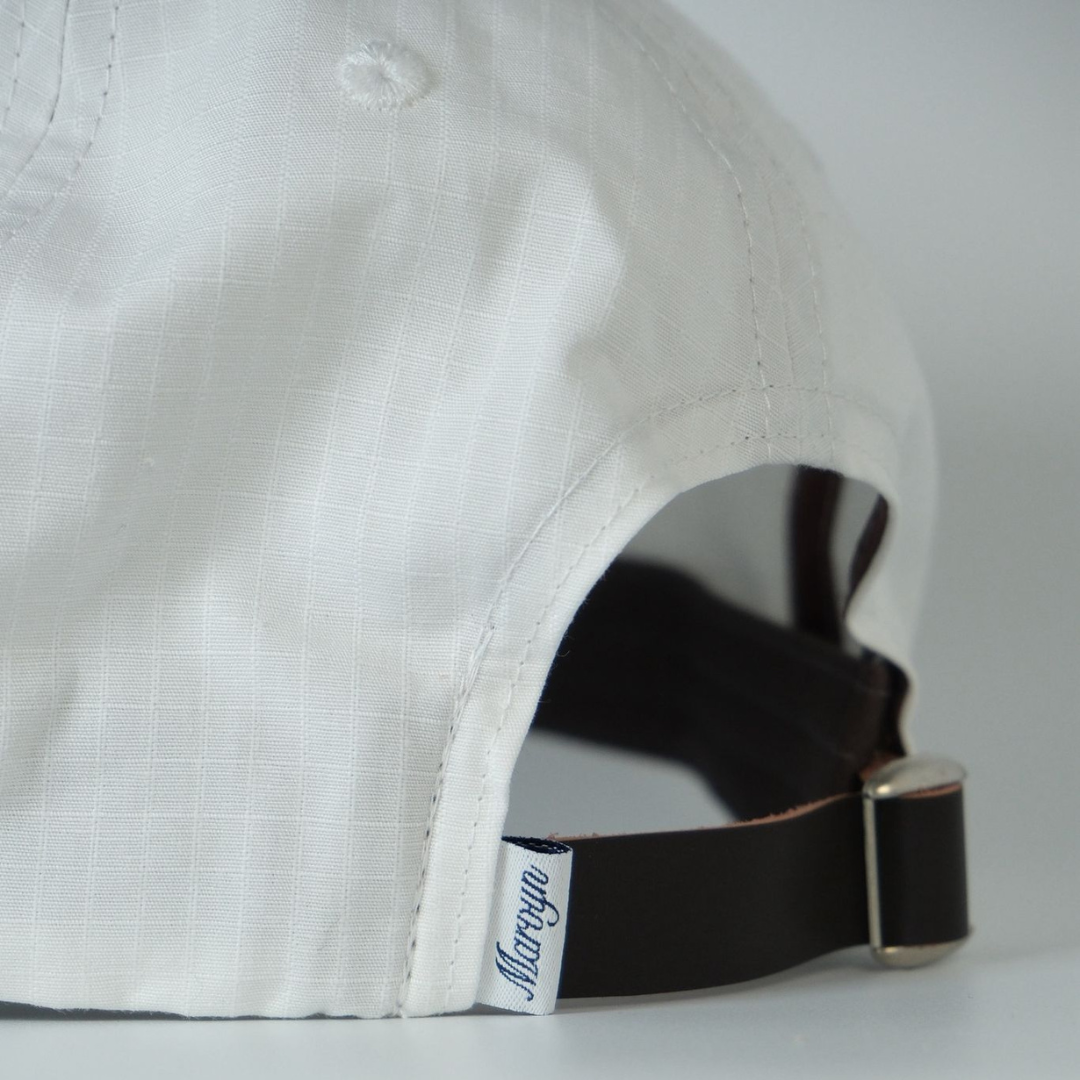 Close-up of a white cap with a black strap and visible brand logo on a light gray background
