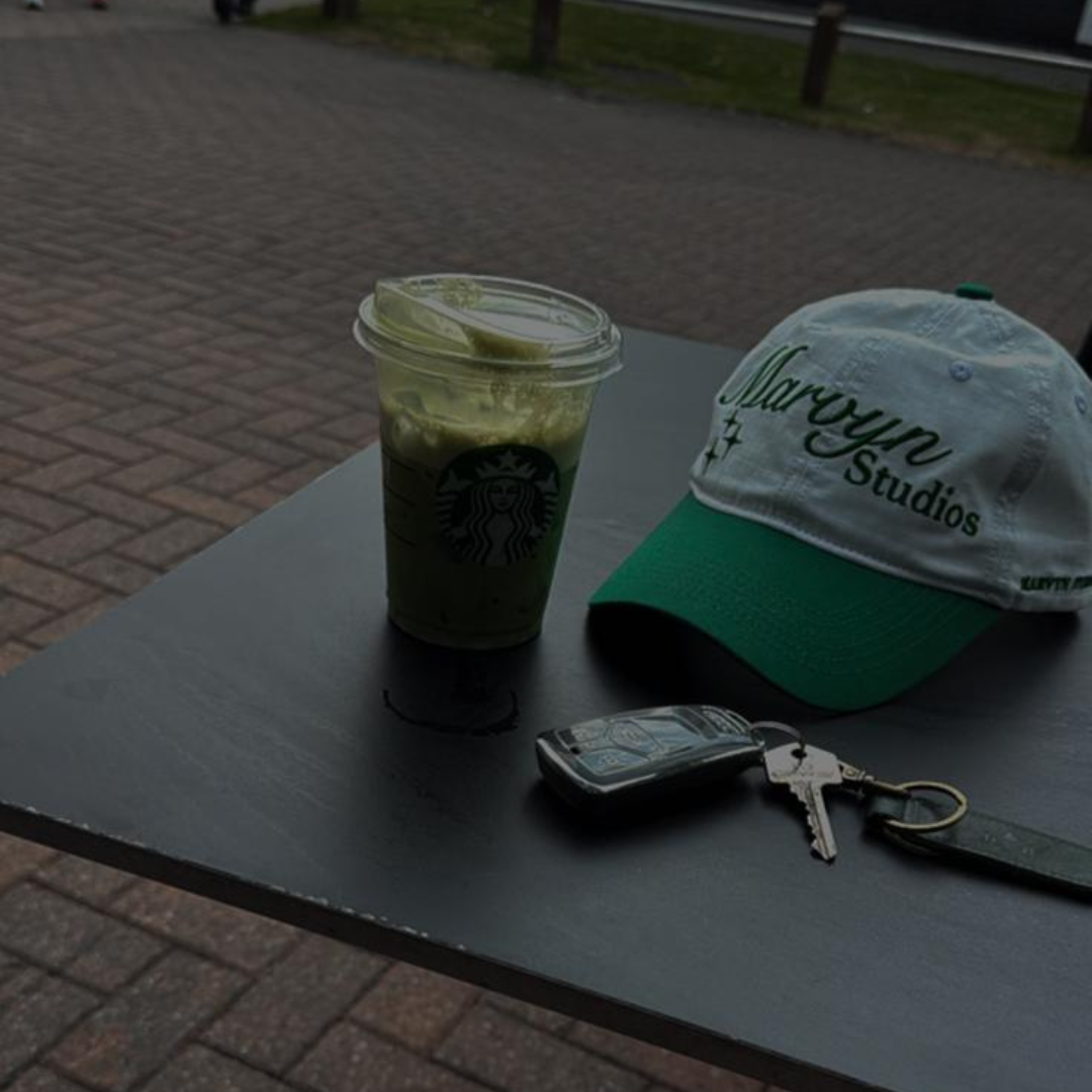Starbucks drink with a lime wedge, a cap, keys, and phone on a table outdoors.