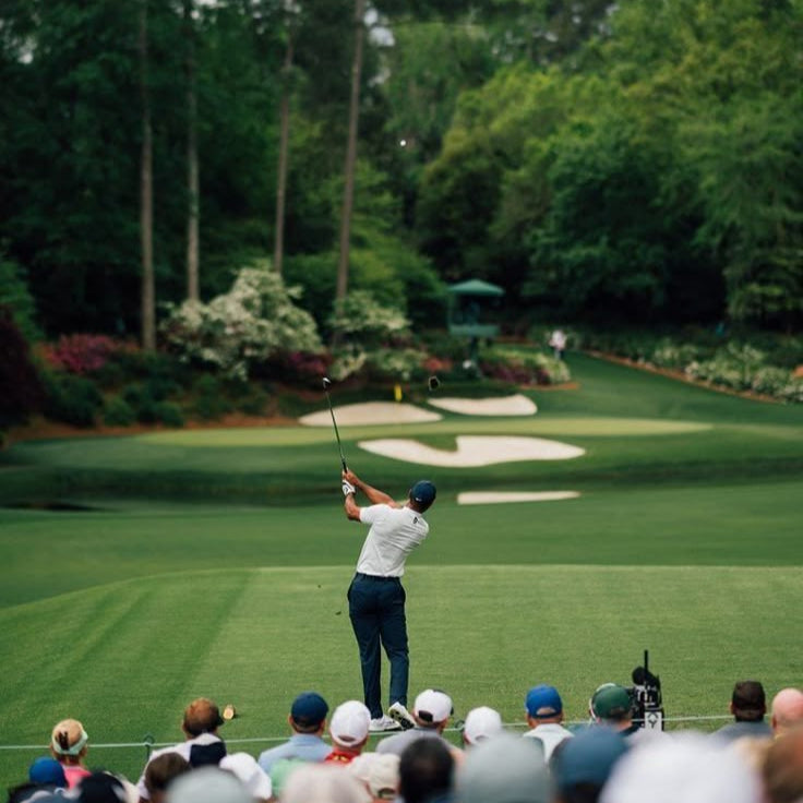 Golfer swinging a club on a golf course with spectators watching.