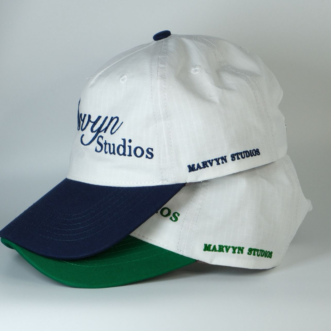 Two baseball caps with 'Marvyn Studios' branding on a light gray background